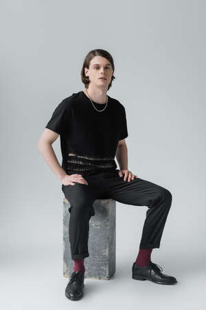 Stylish man sitting on concrete block on grey background