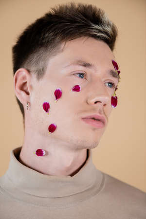 Portrait of young man with petals on face looking away isolated on beigeの写真素材