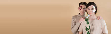 Homosexual man with petals on face hugging boyfriend with eustoma isolated on beige, bannerの写真素材