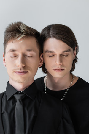Portrait of young homosexual couple standing with closed eyes isolated on greyの写真素材