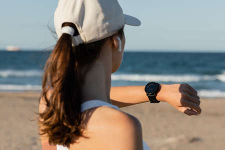 back view of brunette woman in baseball cap checking fitness tracker