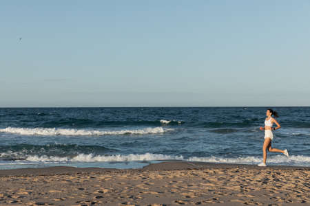 full length of young sportive woman jogging near sea in summerの写真素材