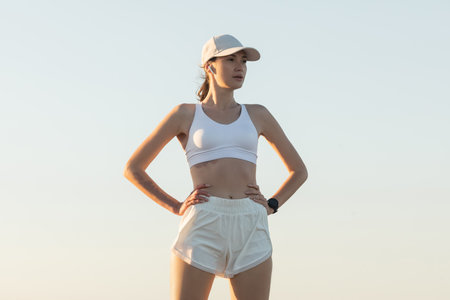 sportive woman in baseball cap and wireless earphone standing with hands on hipsの写真素材