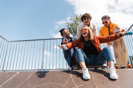 excited woman with soda can screaming on ramp in skate park near interracial friends
