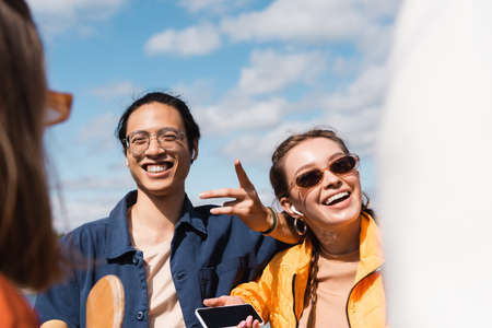 cheerful asian man pointing with finger near smiling woman in stylish sunglassesの写真素材