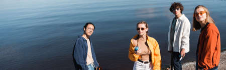 young woman holding soda can near multicultural friends and river, bannerの写真素材