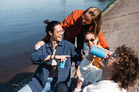 blurred man drinking soda near happy multicultural friends on embankmentの写真素材