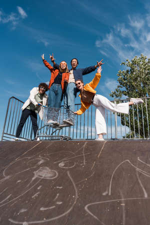 low angle view of cheerful multicultural friends with shopping cart having fun on skate rampの写真素材