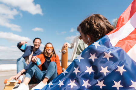 young woman holding usa flag near blurred multicultural friends outdoorsの写真素材