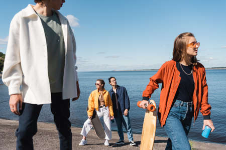woman with longboard and soda can near multiethnic friends on river bankの写真素材