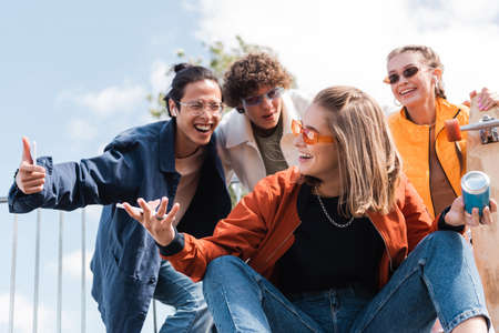 excited asian man showing thumb up near cheerful friend with soda canの写真素材