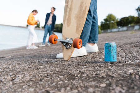 partial view of skater with longboard near soda can and blurred friends on river bankの写真素材