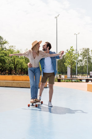 Cheerful couple holding hands and riding longboard in skate parkの写真素材