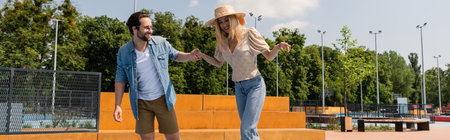 Smiling man holding hand of girlfriend in skate park, banner
