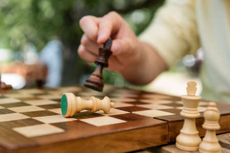 Cropped view of blurred man holding chess figure near board outdoors