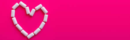 Top view of heart symbol from chewing gums on pink background, banner