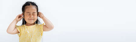 pleased asian girl with closed eyes wearing wired earphones isolated on grey, banner