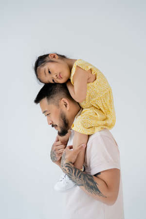 asian father with beard holding preschooler daughter on shoulders isolated on greyの写真素材