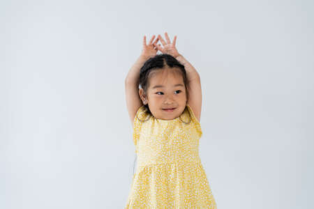 portrait of pleased preschooler and asian girl standing with hands above head isolated on greyの写真素材