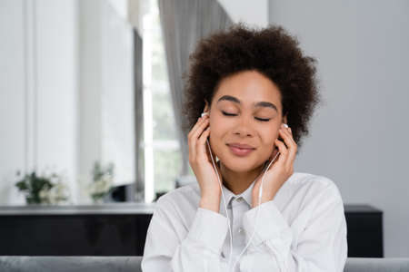 happy african american woman with closed eyes listening music in wired earphones