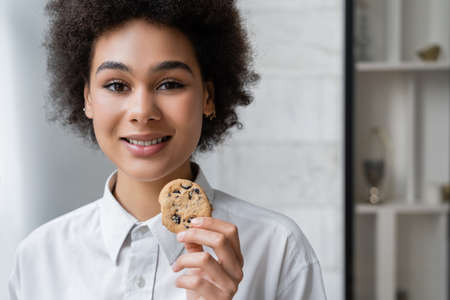 happy african american woman holding cookie with chocolate chipsの写真素材