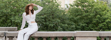 Fashionable woman in sun hat closing eyes on urban street in Paris, bannerの写真素材