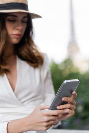 Blurred young woman in sun hat using smartphone outdoors in Parisの写真素材