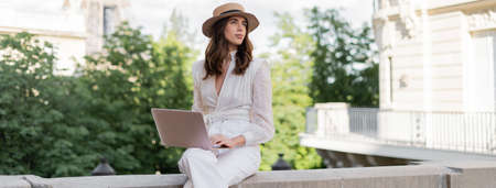 Freelancer in sun hat using laptop on urban street in Paris, bannerの写真素材