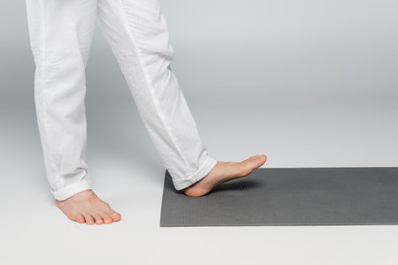 cropped view of barefoot guru man stepping on yoga mat on greyの写真素材