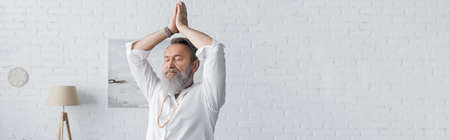 senior bearded man in white shirt meditating with arms up and praying hands, bannerの写真素材