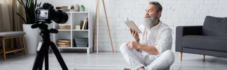 bearded yoga coach reading manual in front of digital camera at home, banner