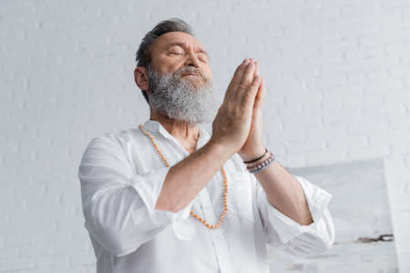 low angle view of bearded guru man meditating with closed eyes and praying hands