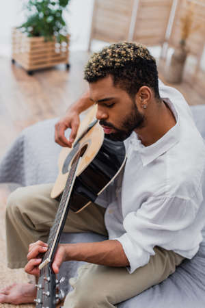 high angle view of african american man with dyed hair playing acoustic guitar at homeの写真素材