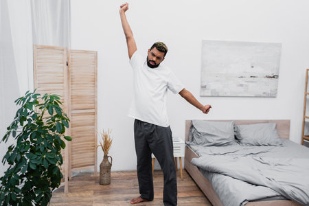 bearded african american man stretching near folding screen in modern bedroomの写真素材