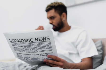 blurred african american man with dyed hair drinking coffee while holding newspaper in bedの写真素材