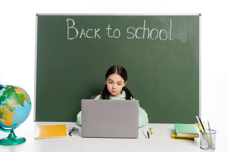 Schoolchild using laptop near books and chalkboard with back to school lettering isolated on whiteの写真素材