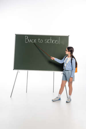 Side view of schoolkid holding pointer near back to school lettering on chalkboard on white backgroundの写真素材