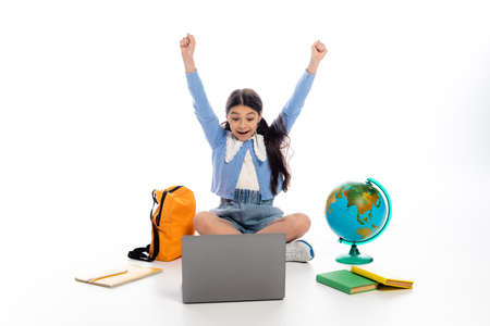Excited schoolchild looking at laptop near books and laptop on white backgroundの写真素材