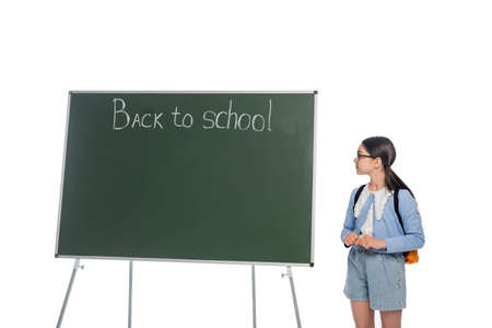 Side view of schoolkid in eyeglasses looking at chalkboard with back to school lettering isolated on whiteの写真素材