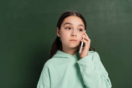 Preteen pupil talking on cellphone near chalkboard at backgroundの写真素材