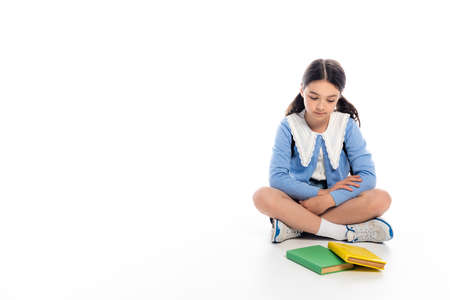 Schoolkid looking at books while sitting on white backgroundの写真素材