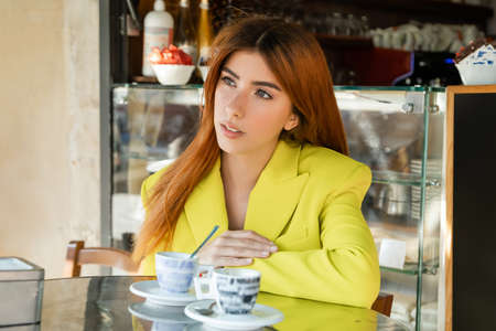 pensive redhead woman looking away near coffee cups on cafe terrace in Veniceの写真素材