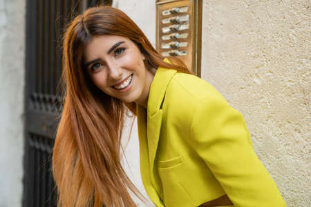 cheerful and stylish woman with red hair looking at camera on street in Venice
