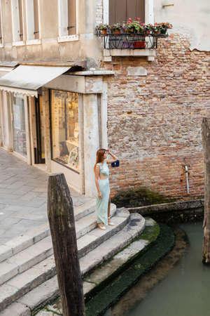 full length of elegant woman standing on stairs near city canal in Veniceの写真素材