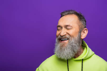 joyful senior man with beard and grey hair smiling with closed eyed on purpleの写真素材