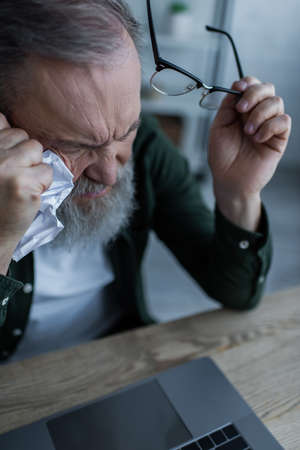 high angle view of bearded senior man holding eyeglasses and crumpled paper near laptopの写真素材