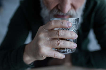 cropped view of senior man drinking whiskey while holding glass