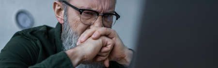 stressed senior man in eyeglasses frowning and covering face with clenched hands, bannerの写真素材