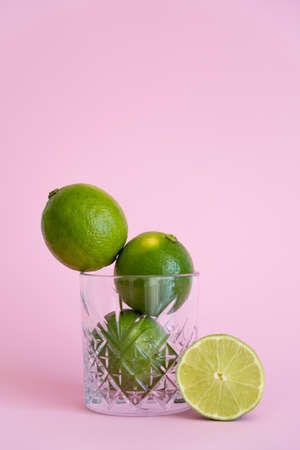 green fresh citrus fruit in faceted glass near half of lime on pinkの写真素材