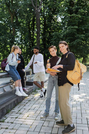 Happy students holding notebooks near blurred multicultural friends in parkの写真素材